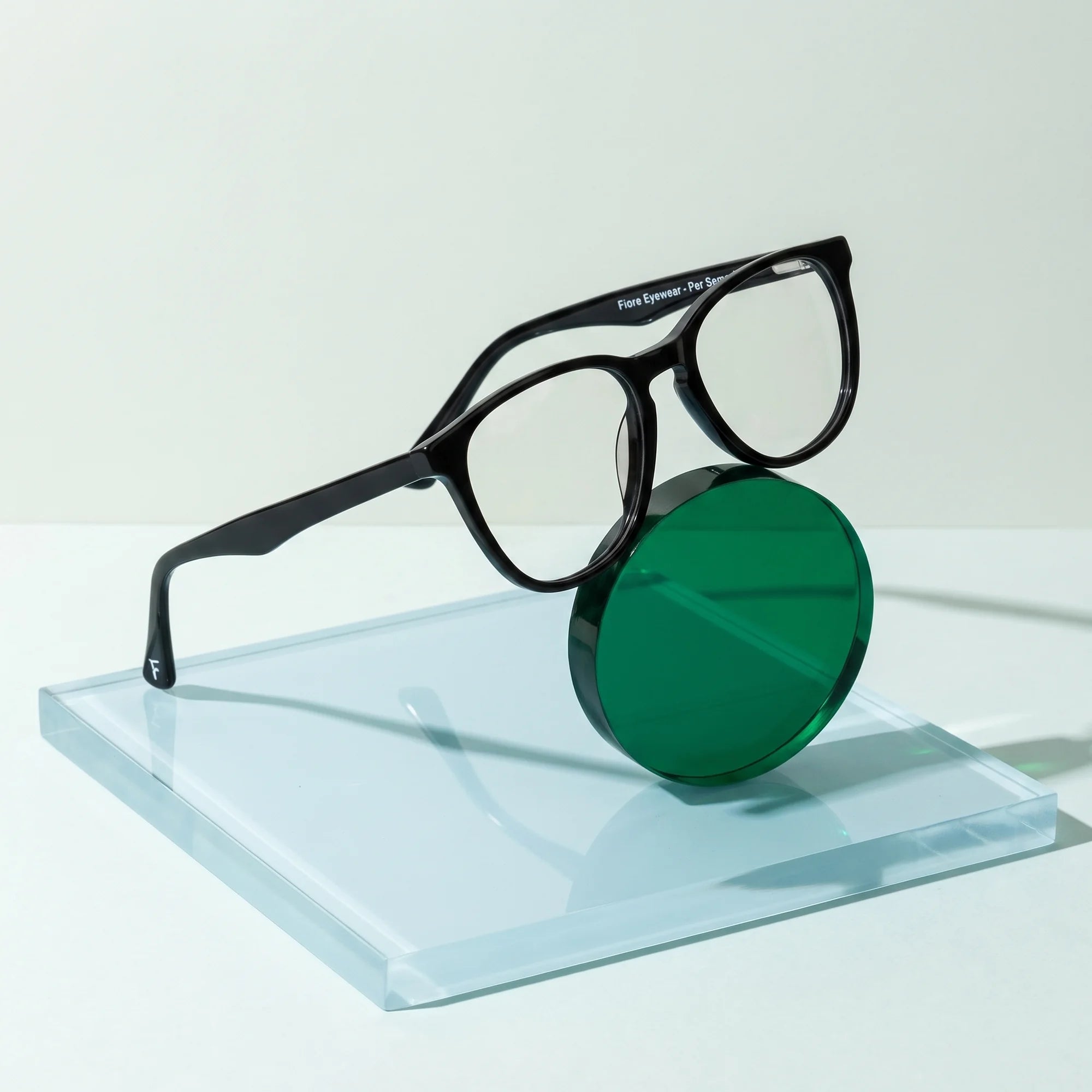 Fiore 7046 eyeglasses in black – on a cobalt acrylic disc in soft daylight