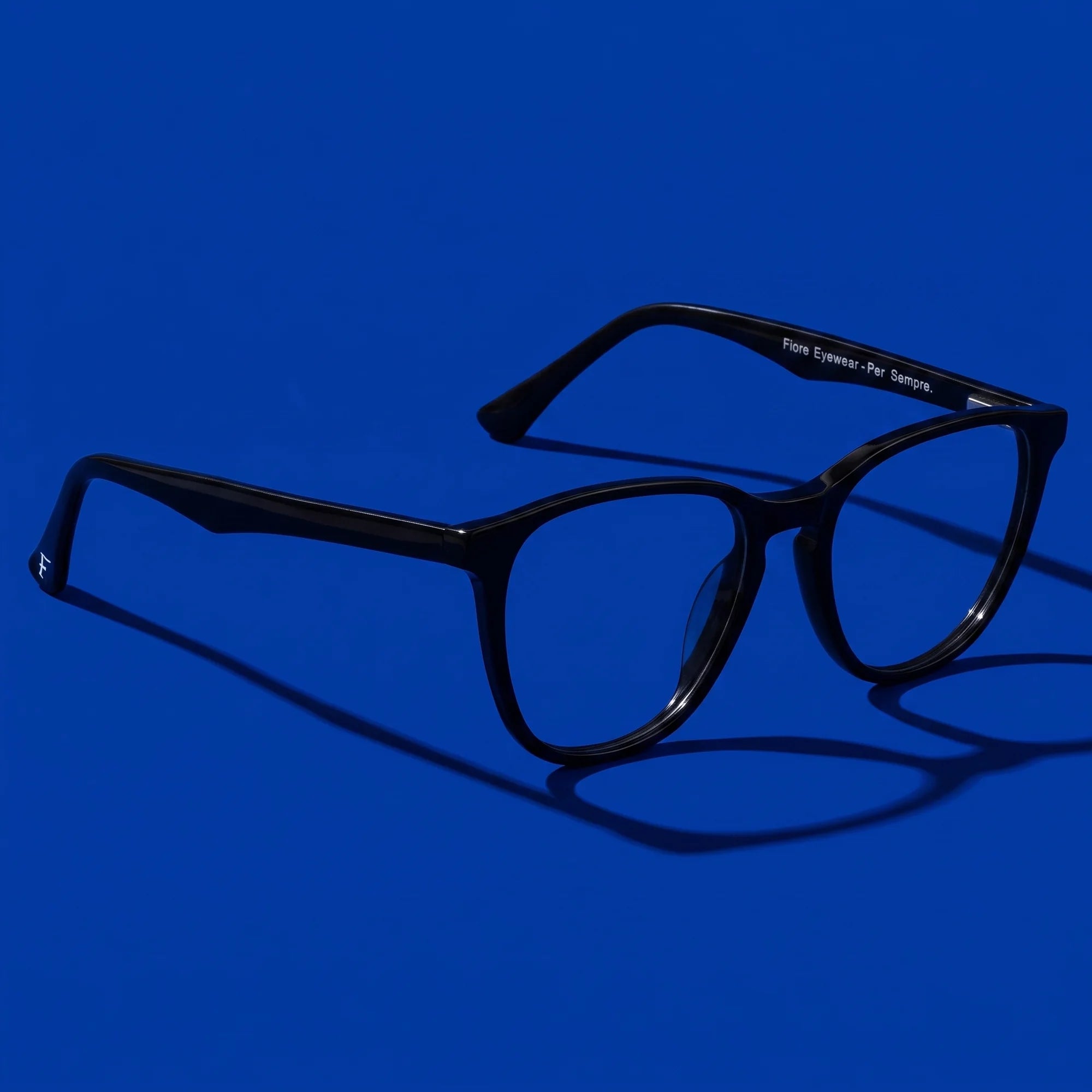 Fiore 7046 eyeglasses in black – hero still life against a deep cobalt backdrop