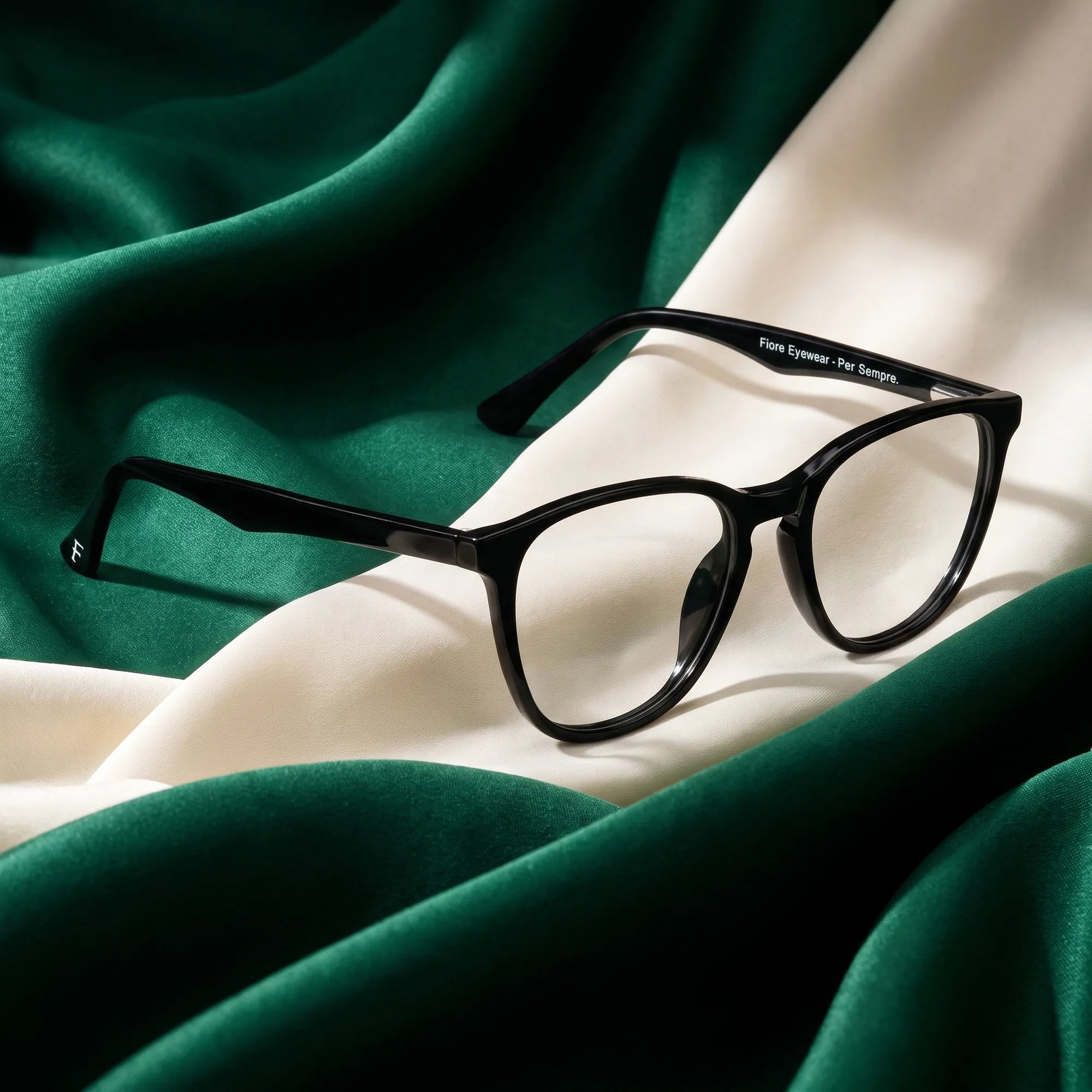 Fiore 7046 eyeglasses in black – resting on draped emerald and ivory silk