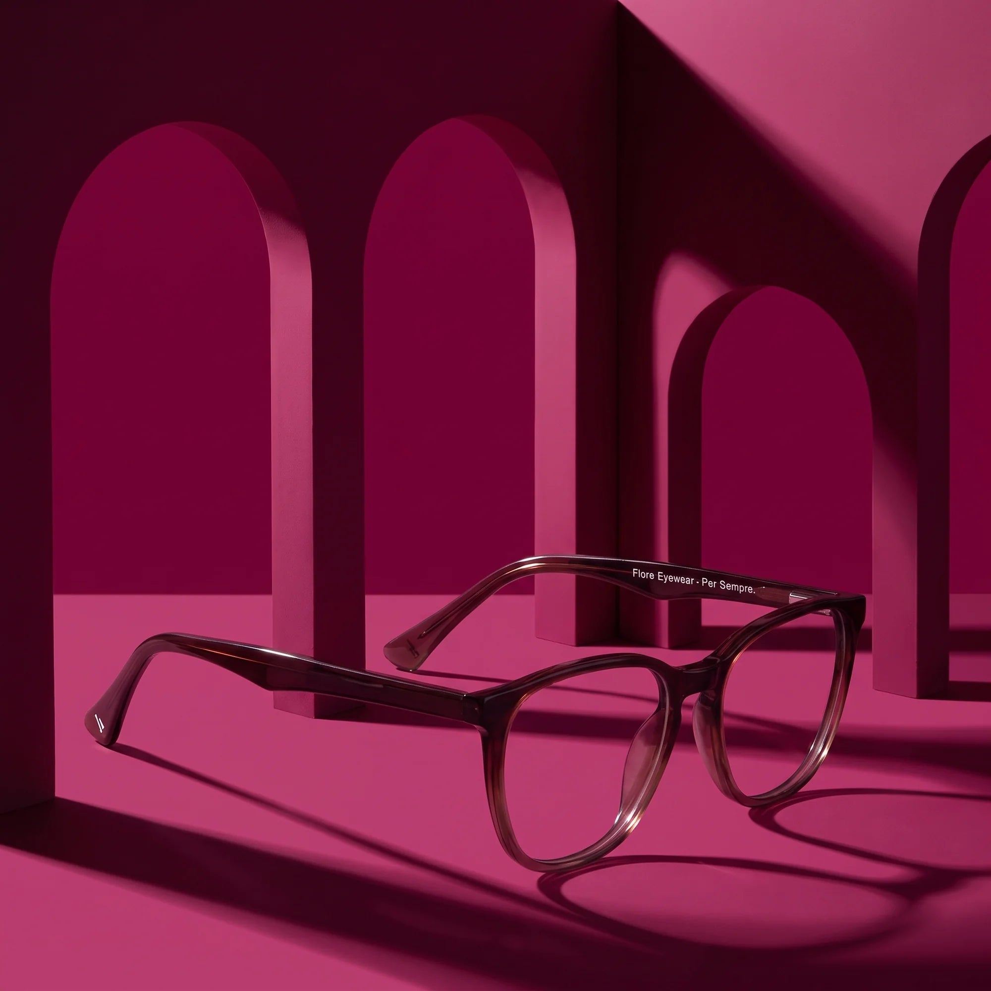 Fiore 7046 eyeglasses in gradual brown – displayed on a magenta podium among arches