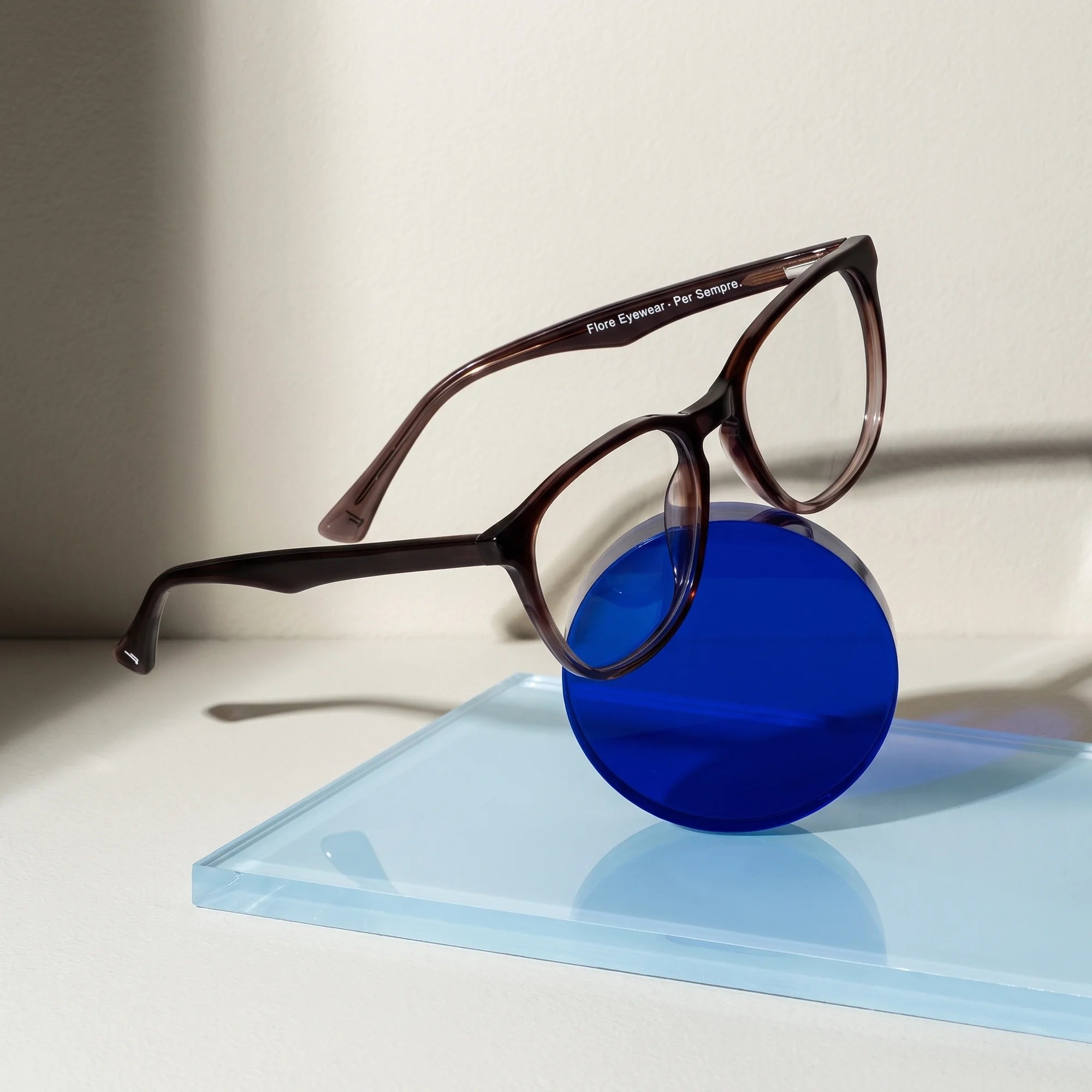 Fiore 7046 eyeglasses in gradual brown – on a cobalt acrylic disc in soft daylight