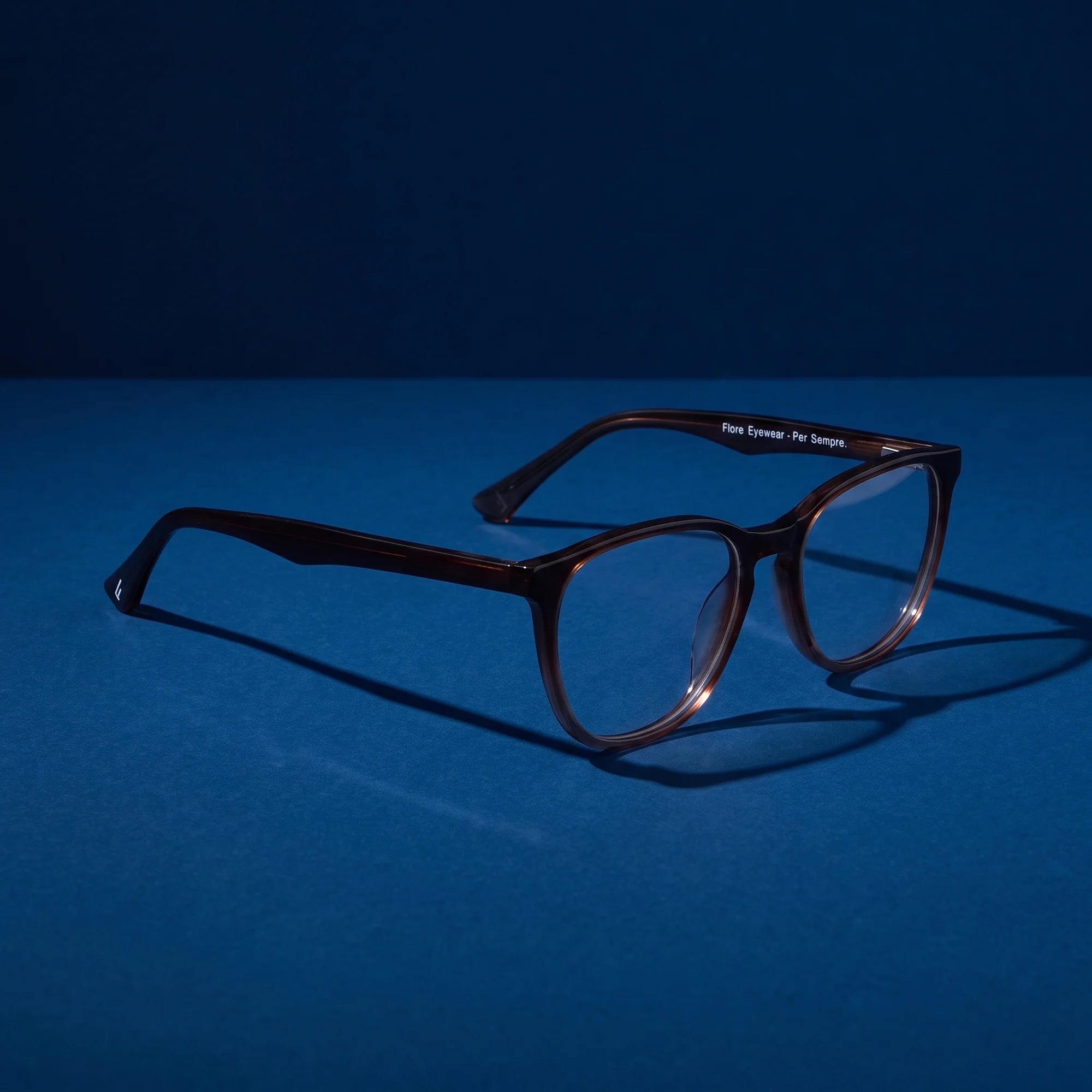 Fiore 7046 eyeglasses in gradual brown – hero still life against a deep midnight blue backdrop