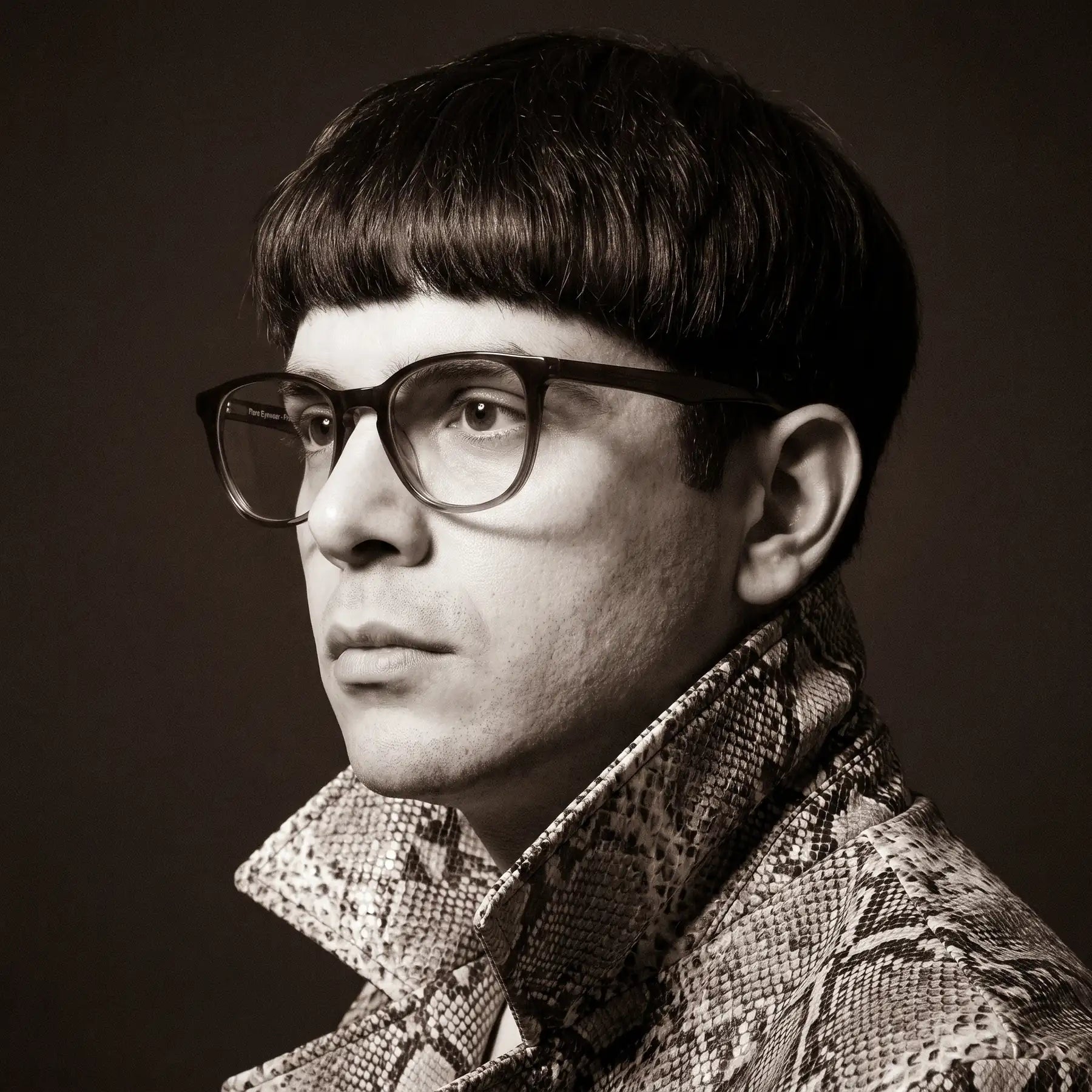 Fiore 7046 eyeglasses in gradual brown, worn by a model – campaign portrait, monochrome studio portrait, red graphic accents