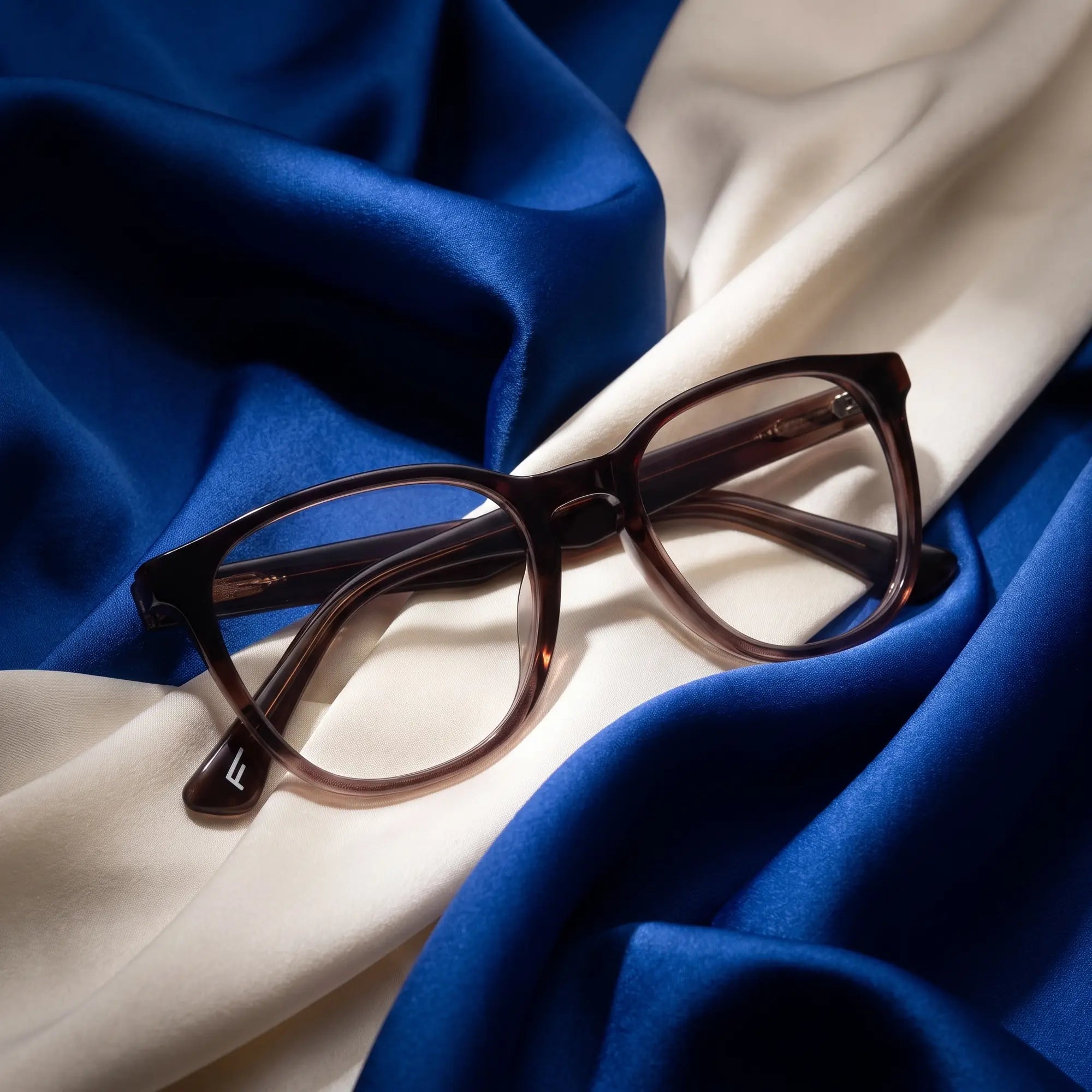 Fiore 7046 eyeglasses in gradual brown – resting on draped cobalt and ivory silk