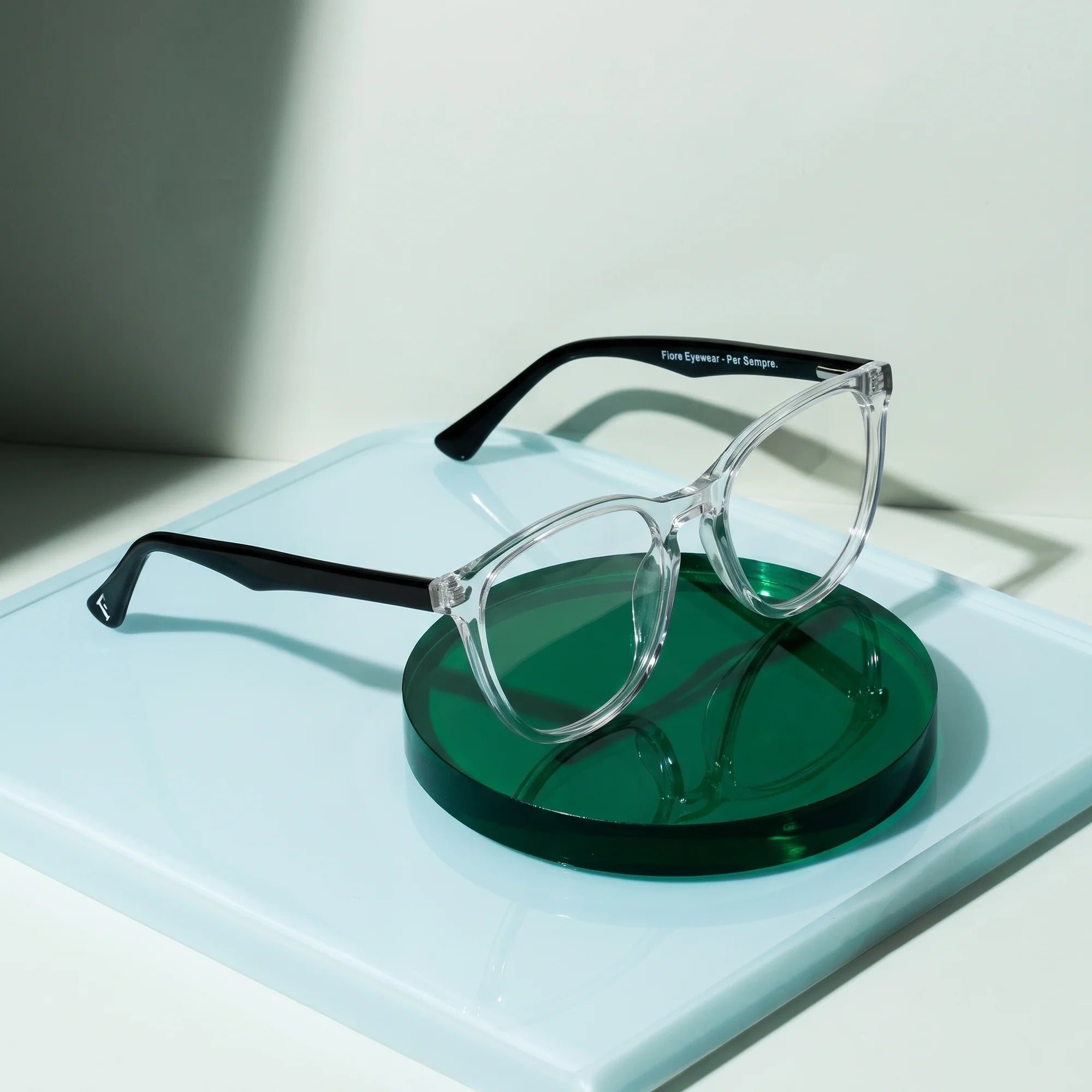 Fiore 7046 eyeglasses in transparent – on a cobalt acrylic disc in soft daylight
