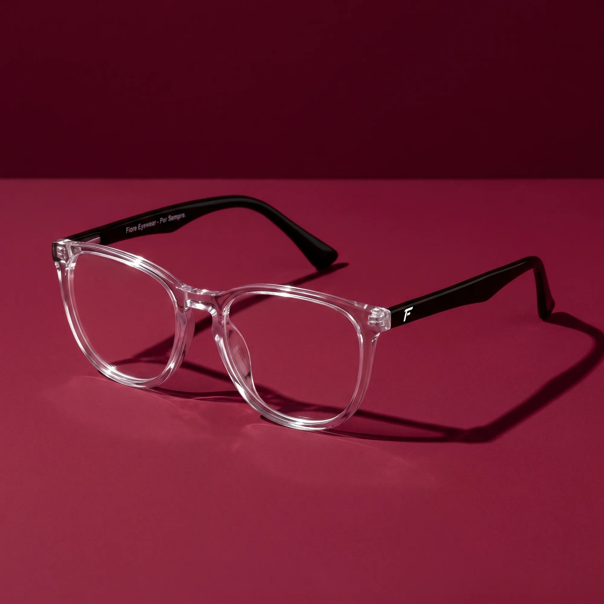 Fiore 7046 eyeglasses in transparent – editorial still life on a saturated burgundy set