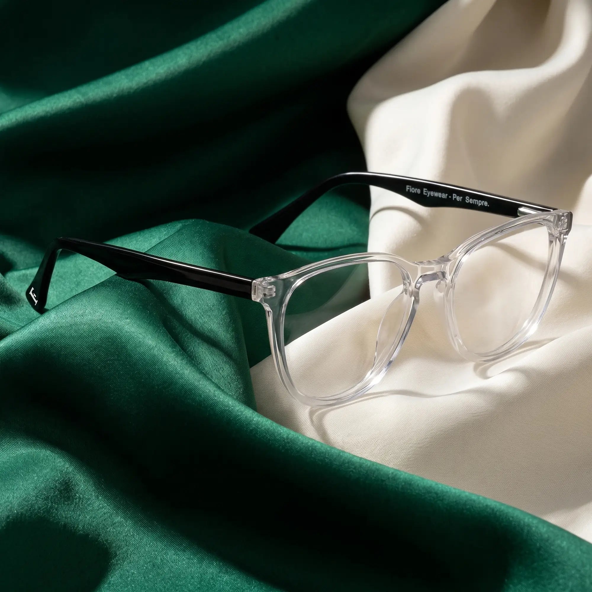 Fiore 7046 eyeglasses in transparent – resting on draped emerald and ivory silk